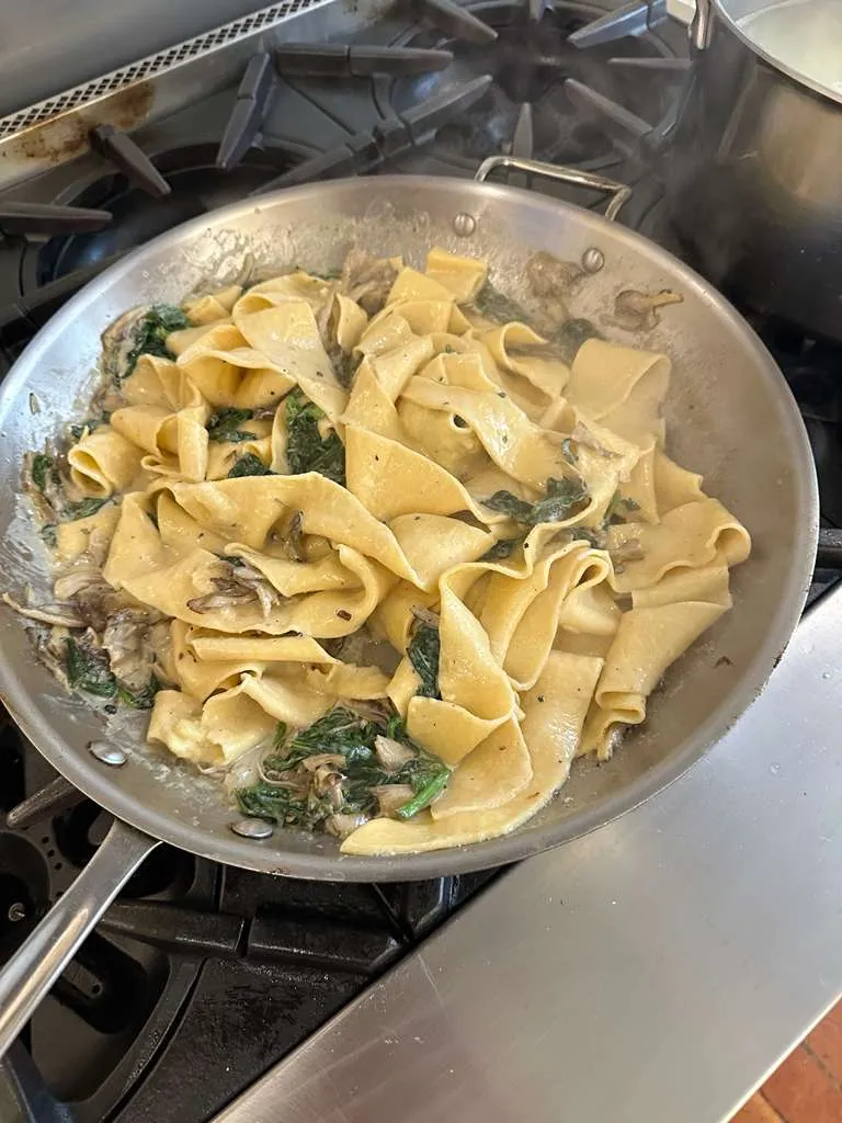 Fresh pappardelle pasta with maitake mushrooms and greens in a sauté pan